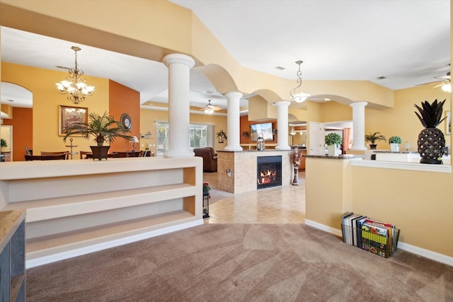 reception with ceiling fan with notable chandelier, a tile fireplace, and decorative columns