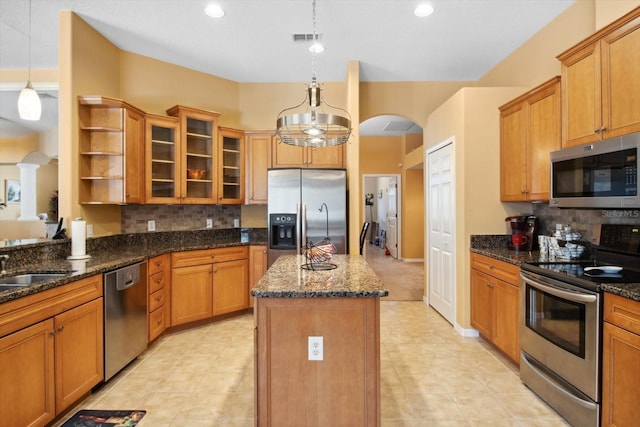 kitchen with decorative light fixtures, an island with sink, backsplash, appliances with stainless steel finishes, and dark stone countertops