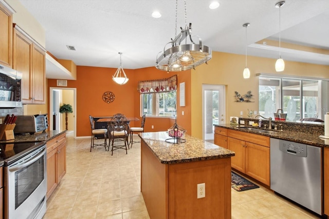 kitchen featuring a kitchen island, stainless steel appliances, dark stone countertops, and hanging light fixtures