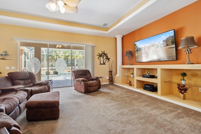 carpeted living room featuring a raised ceiling, built in features, ceiling fan, and ornate columns