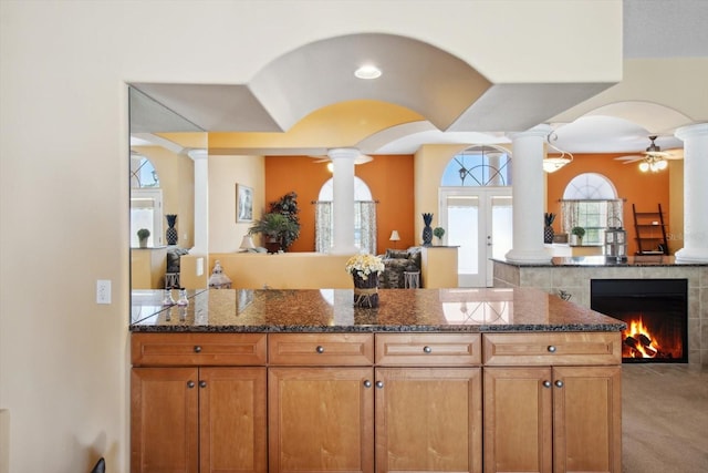 kitchen featuring a fireplace, ceiling fan, and dark stone countertops