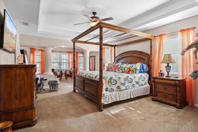 bedroom with a raised ceiling, ceiling fan, light carpet, and ornate columns