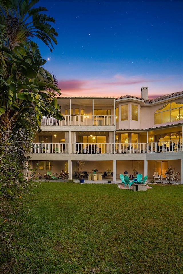 back house at dusk with a lawn and a patio