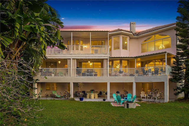 back house at dusk with a balcony, a patio, and a yard