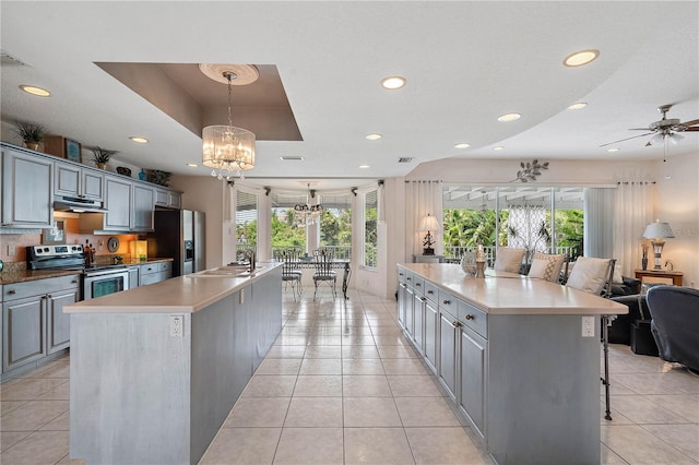 kitchen featuring a raised ceiling, appliances with stainless steel finishes, gray cabinets, and a spacious island