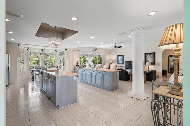 kitchen with sink, stainless steel fridge, a raised ceiling, a kitchen island with sink, and decorative columns