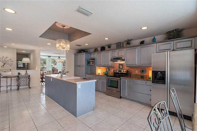 kitchen featuring appliances with stainless steel finishes, a kitchen island with sink, sink, gray cabinets, and a tray ceiling