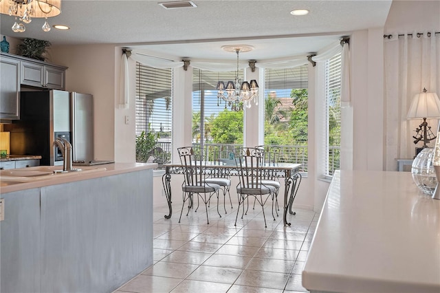 dining area with sink, light tile patterned flooring, a textured ceiling, and a notable chandelier