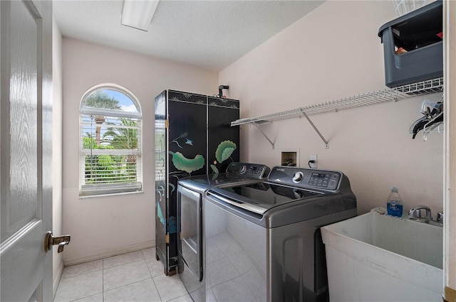 laundry room featuring sink, washer and clothes dryer, a textured ceiling, and light tile patterned flooring