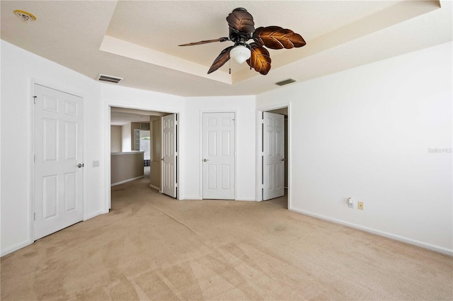 unfurnished bedroom with light colored carpet, a raised ceiling, and ceiling fan