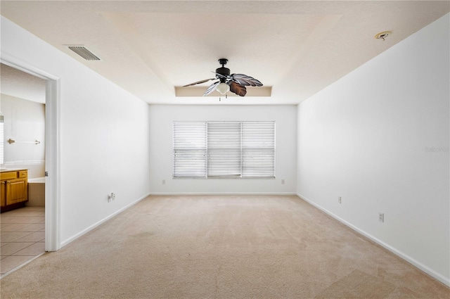 spare room featuring a raised ceiling, light colored carpet, and ceiling fan