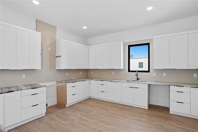 kitchen featuring light stone countertops, light wood-type flooring, backsplash, white cabinetry, and sink