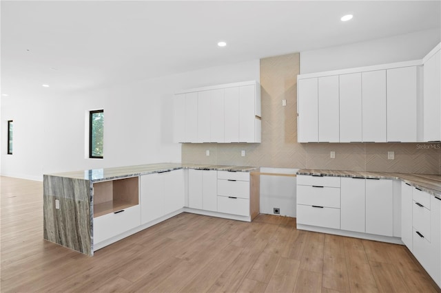 kitchen featuring light hardwood / wood-style floors, kitchen peninsula, light stone countertops, white cabinetry, and tasteful backsplash