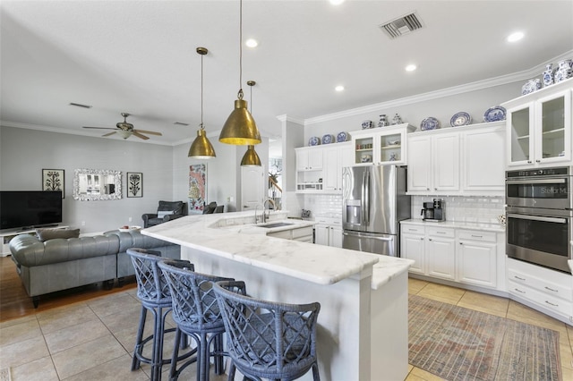 kitchen featuring white cabinetry, appliances with stainless steel finishes, decorative light fixtures, a kitchen breakfast bar, and light stone counters