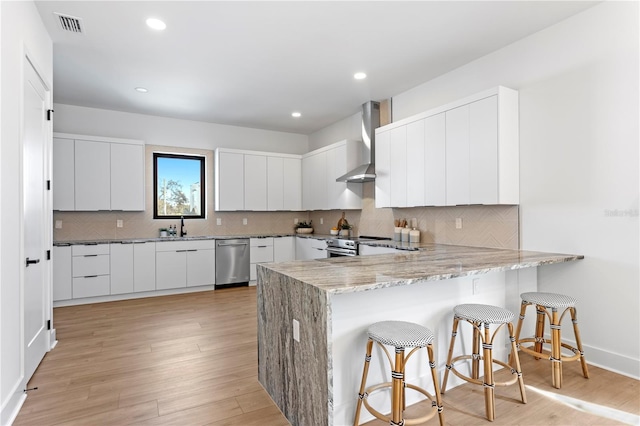 kitchen featuring stainless steel appliances, wall chimney range hood, a breakfast bar area, white cabinetry, and sink