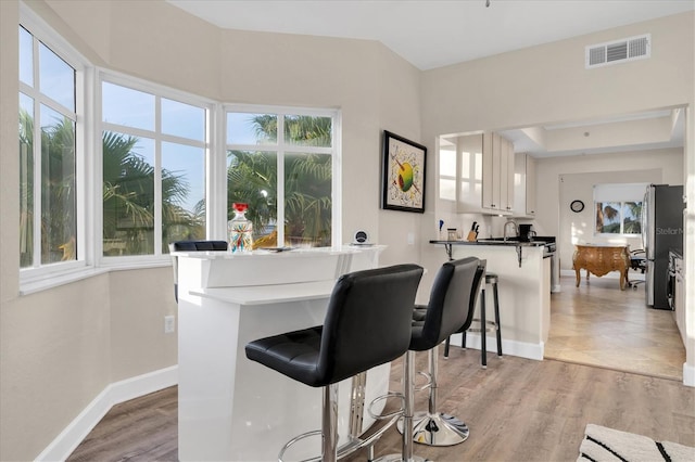 bar with stainless steel refrigerator, light wood-type flooring, and white cabinetry