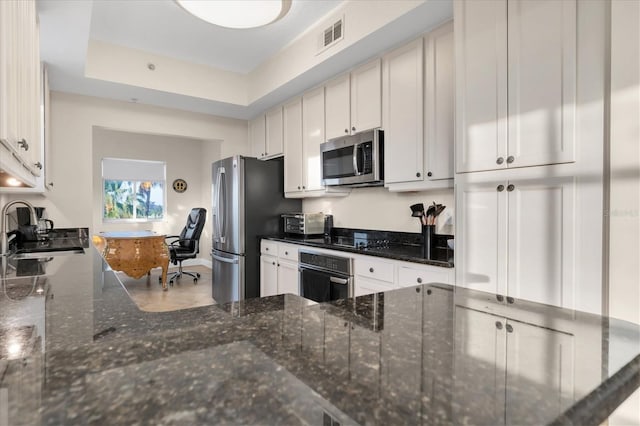 kitchen with sink, stainless steel appliances, dark stone counters, and white cabinetry