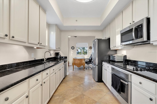 kitchen featuring a raised ceiling, white cabinetry, appliances with stainless steel finishes, dark stone countertops, and sink