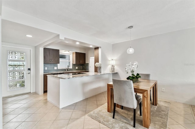 kitchen with backsplash, dark brown cabinets, light stone countertops, a healthy amount of sunlight, and kitchen peninsula