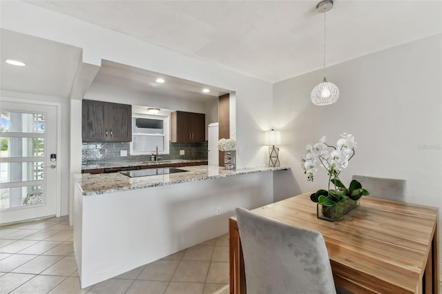 kitchen featuring dark brown cabinets, light stone counters, decorative backsplash, decorative light fixtures, and kitchen peninsula