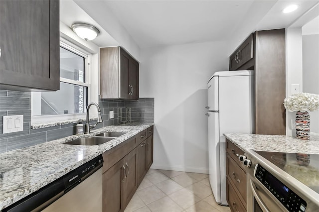 kitchen with light tile patterned flooring, sink, appliances with stainless steel finishes, light stone countertops, and backsplash