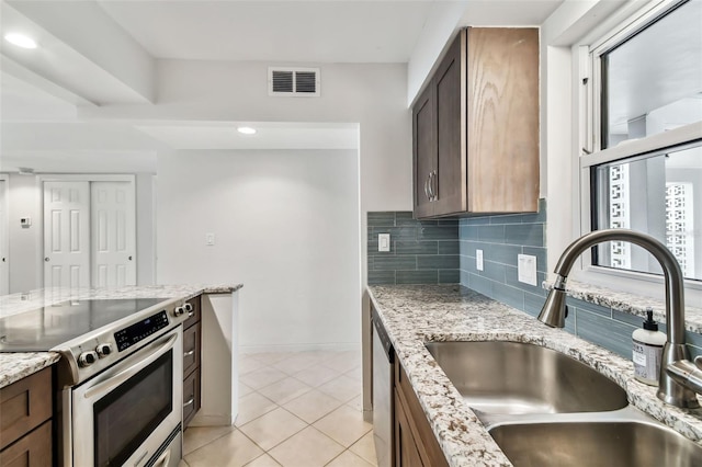 kitchen with appliances with stainless steel finishes, sink, decorative backsplash, light tile patterned floors, and light stone counters