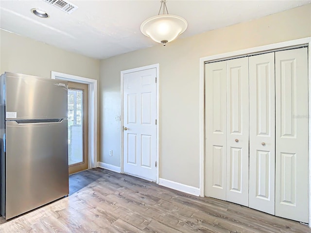 kitchen with hanging light fixtures, stainless steel refrigerator, and light hardwood / wood-style flooring