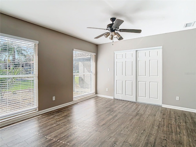 unfurnished bedroom featuring multiple windows, dark hardwood / wood-style floors, ceiling fan, and a closet