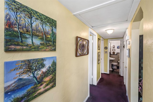 corridor with carpet, a textured wall, and baseboards