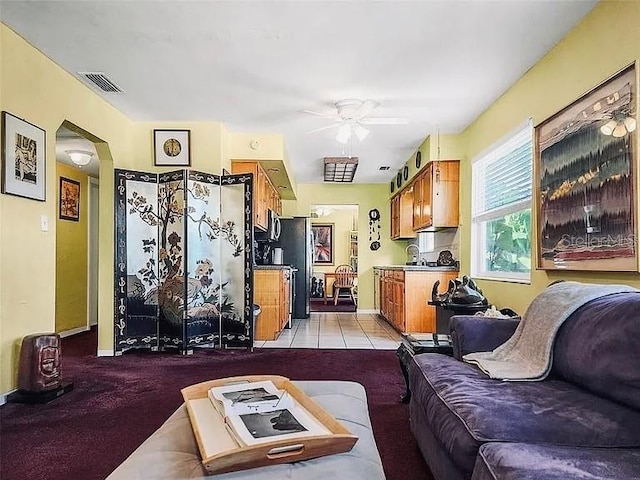 living room featuring light tile patterned floors, visible vents, arched walkways, and ceiling fan