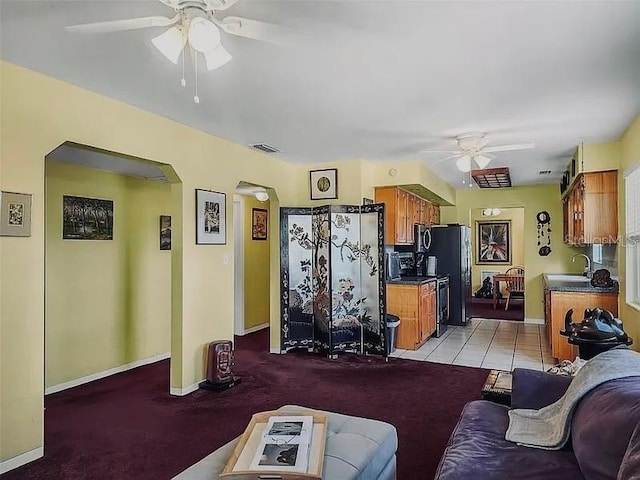 living room with light tile patterned floors, a ceiling fan, visible vents, baseboards, and arched walkways