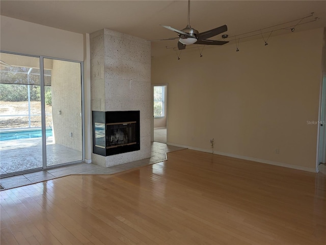 unfurnished living room featuring a high ceiling, a multi sided fireplace, ceiling fan, and light wood-type flooring