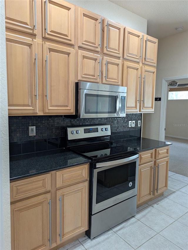 kitchen featuring dark stone countertops, light tile patterned floors, backsplash, and stainless steel appliances