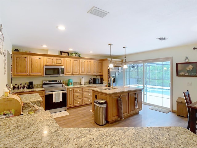 kitchen featuring decorative light fixtures, sink, a kitchen island with sink, appliances with stainless steel finishes, and light wood-type flooring