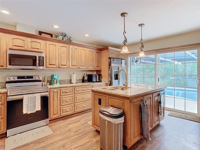 kitchen with hanging light fixtures, a kitchen island with sink, light wood-type flooring, stainless steel appliances, and light stone counters