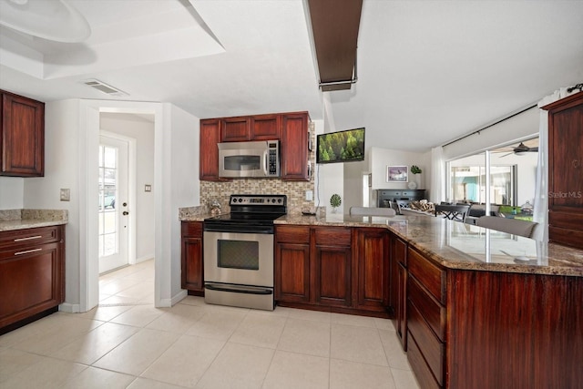 kitchen with light tile patterned floors, appliances with stainless steel finishes, kitchen peninsula, light stone countertops, and decorative backsplash