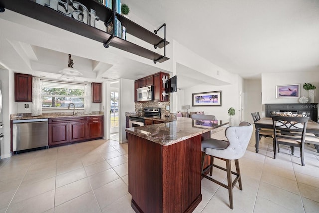 kitchen with sink, light tile patterned floors, stainless steel appliances, a raised ceiling, and dark stone counters