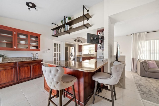 kitchen featuring light tile patterned floors, sink, a breakfast bar area, light stone countertops, and stainless steel fridge with ice dispenser