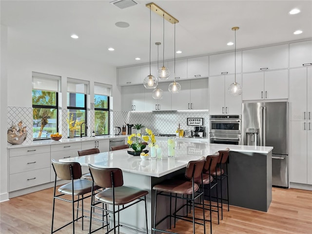 kitchen with a breakfast bar, light wood-style flooring, white cabinetry, stainless steel appliances, and light countertops