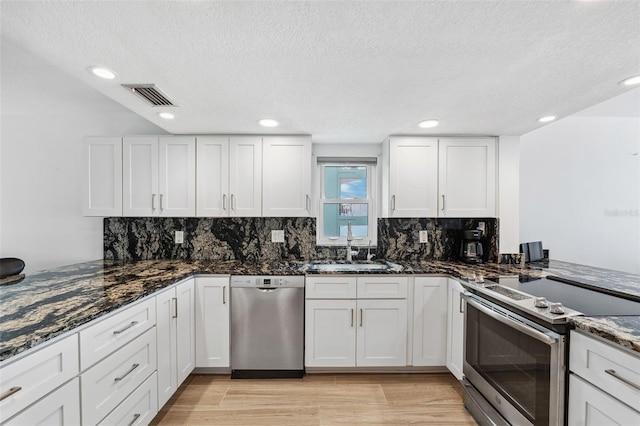 kitchen with a sink, visible vents, white cabinetry, appliances with stainless steel finishes, and dark stone countertops