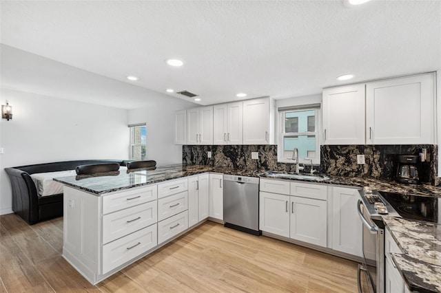 kitchen featuring stainless steel appliances, a peninsula, a sink, white cabinets, and light wood-type flooring