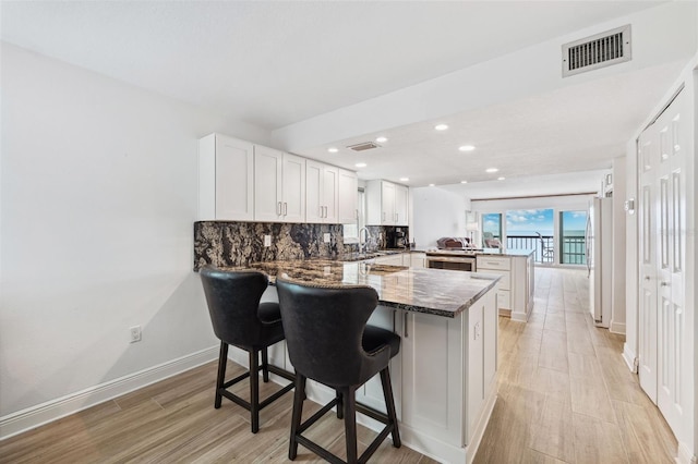 kitchen with visible vents, dark stone counters, decorative backsplash, freestanding refrigerator, and a peninsula