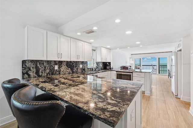 kitchen with a peninsula, visible vents, white cabinetry, backsplash, and freestanding refrigerator