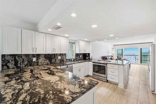 kitchen featuring a peninsula, a sink, white cabinetry, appliances with stainless steel finishes, and tasteful backsplash