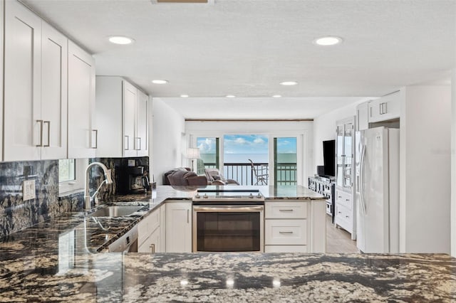 kitchen with dark stone counters, a peninsula, stainless steel electric stove, white fridge with ice dispenser, and a sink