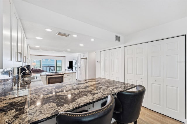 kitchen with a peninsula, white refrigerator with ice dispenser, a sink, visible vents, and white cabinets