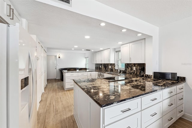 kitchen with light wood-style flooring, a peninsula, white refrigerator with ice dispenser, a sink, and white cabinetry