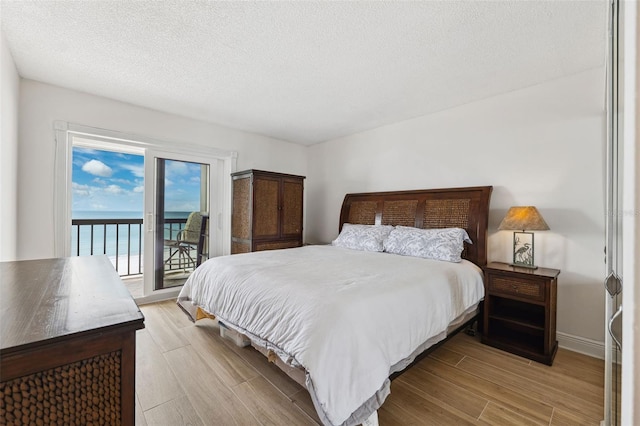 bedroom with baseboards, a water view, access to exterior, a textured ceiling, and light wood-type flooring