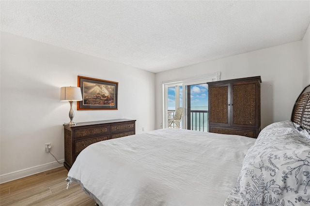 bedroom with access to exterior, baseboards, light wood finished floors, and a textured ceiling