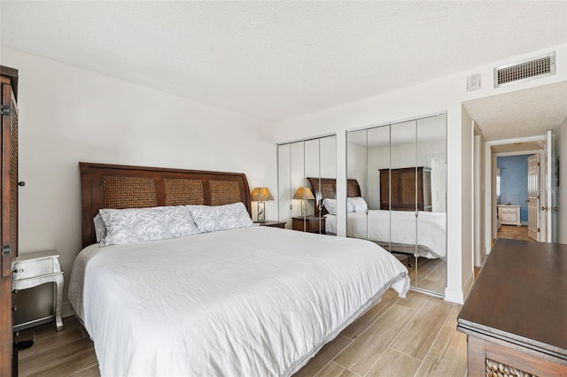 bedroom featuring visible vents, light wood-style flooring, a textured ceiling, and two closets